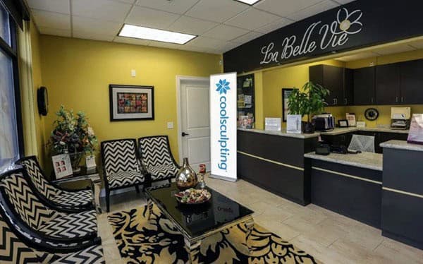 The La Belle Vie waiting area in Draper, with chevron armchairs, a patterned rug and a CoolSculpting banner beside the front desk