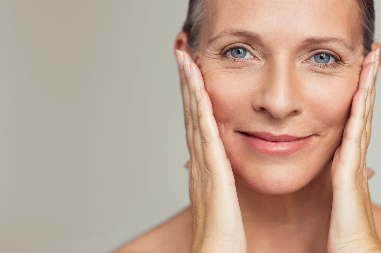 A smiling woman in her fifties with smooth, even skin, her hands framing her face