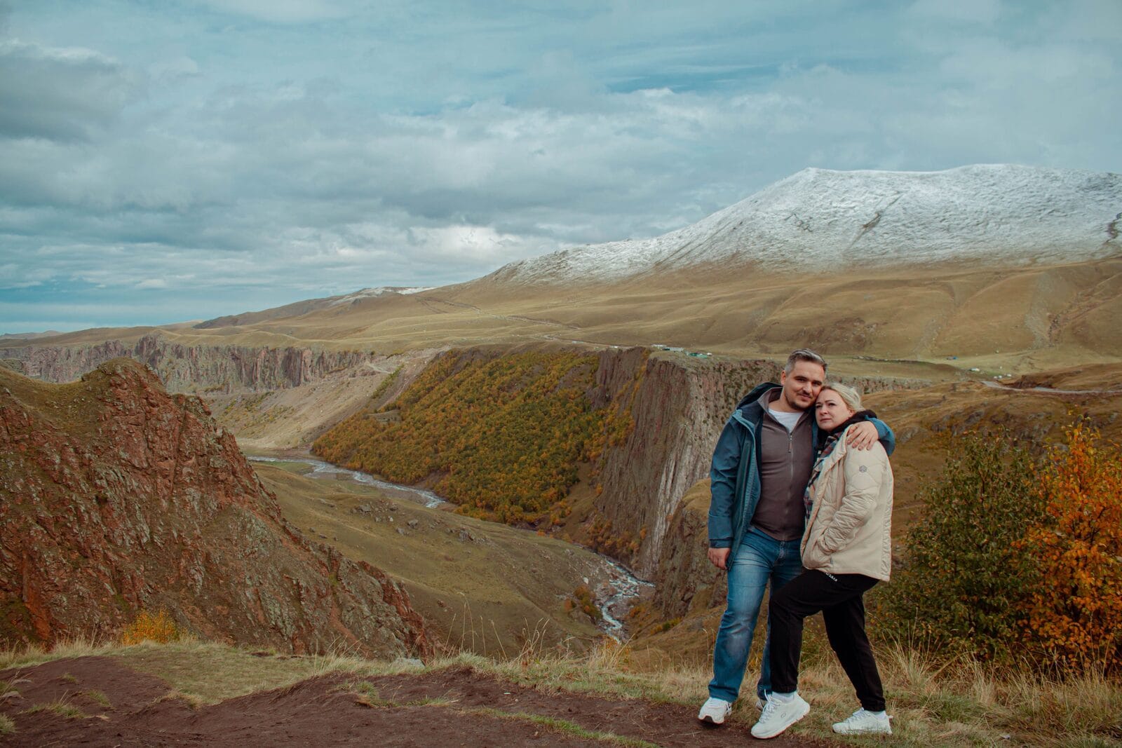 A middle-aged couple standing arm in arm at a mountain canyon overlook