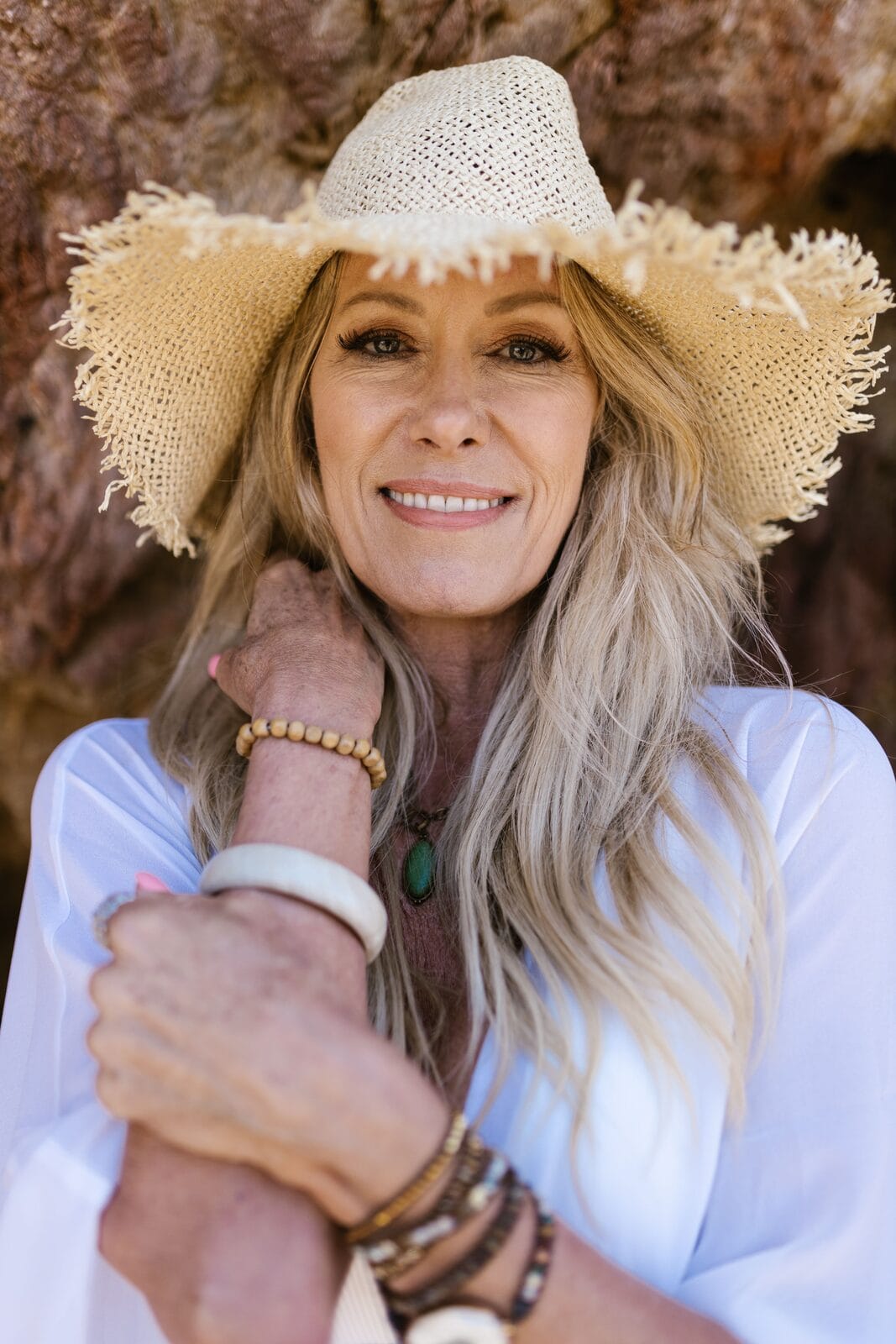 A smiling blonde woman in her fifties in a straw hat, outdoors in warm sunlight