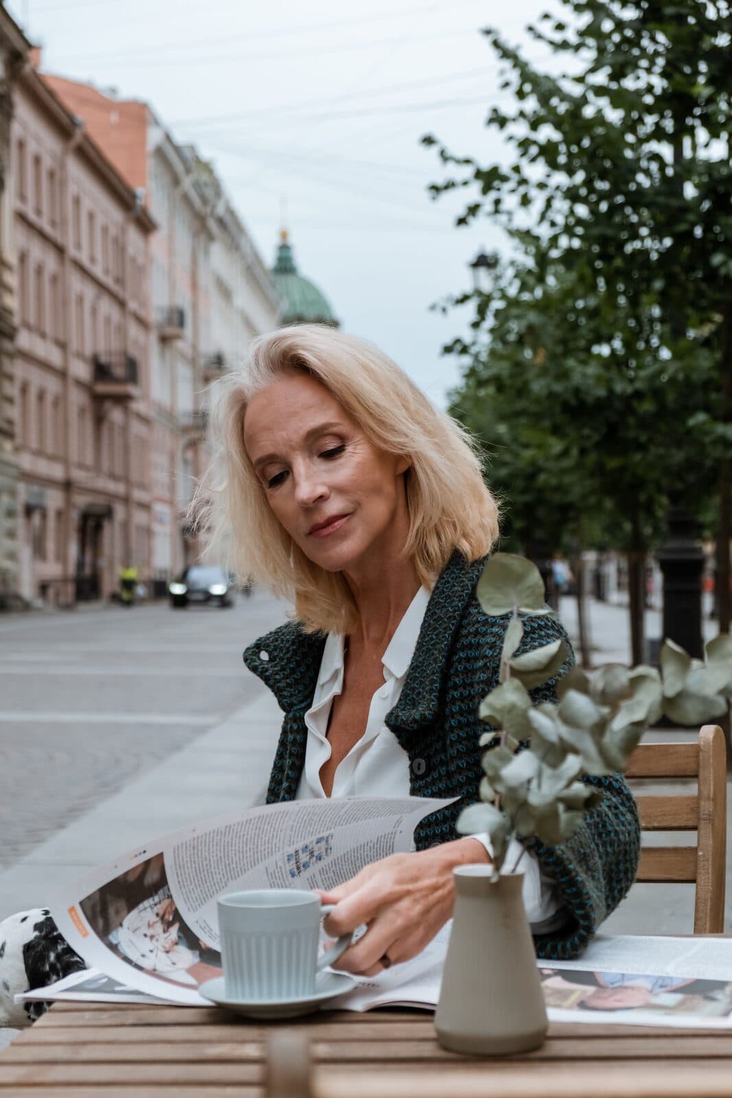 A woman in her fifties with full, shoulder-length blonde hair on a tree-lined street