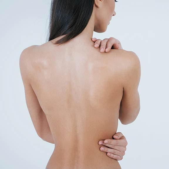 A woman seen from behind with smooth, bare shoulders, one hand on her shoulder