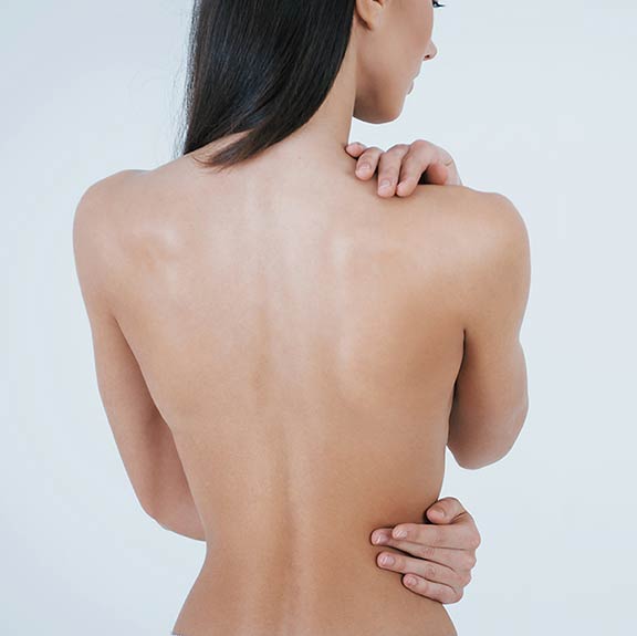 A woman seen from behind with smooth, bare shoulders, one hand on her shoulder
